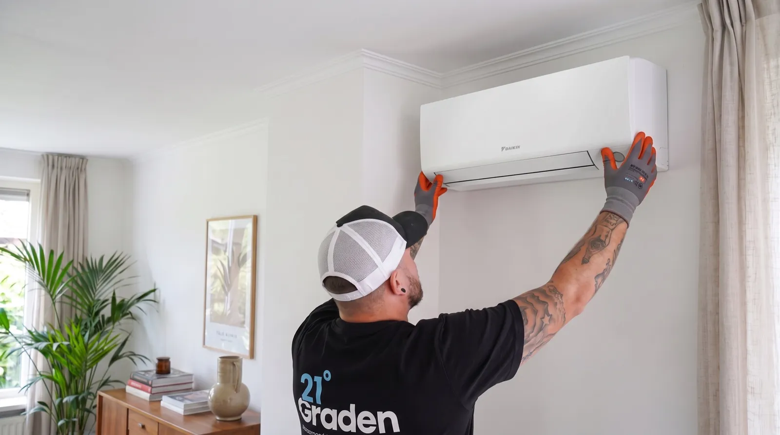 Monteur van 21 Graden hangt een airco op in een woonkamer